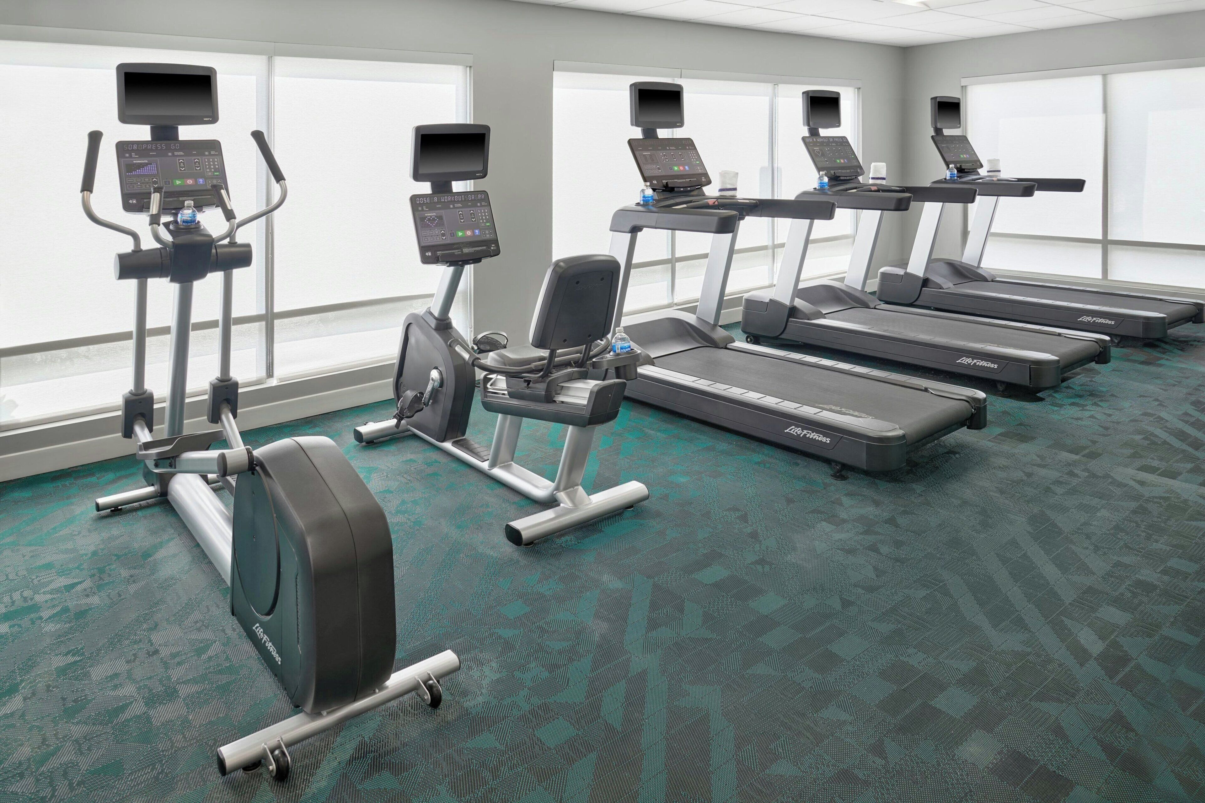 A gym with treadmills, elliptical machines, and stationary bikes, equipped with digital displays.
