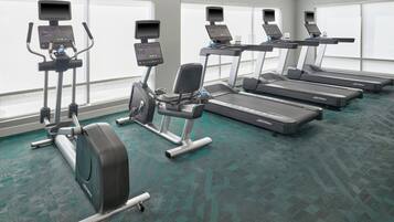 A gym with treadmills, elliptical machines, and stationary bikes, equipped with digital displays.