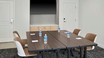 Un salón de conferencias con una mesa larga, seis sillas y botellas de agua sobre la mesa.