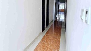 Un couloir aux murs blancs et au sol en marbre mène à une pièce dotée d’une grande fenêtre.
