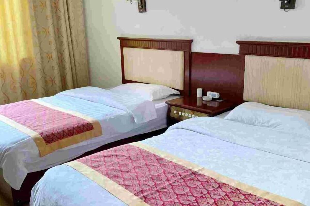 A hotel room with two beds, each with a wooden headboard and a bedside table with a lamp.