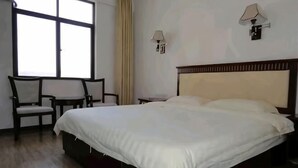 Une chambre d’hôtel avec un grand lit, deux chaises, une petite table et une fenêtre avec des rideaux.