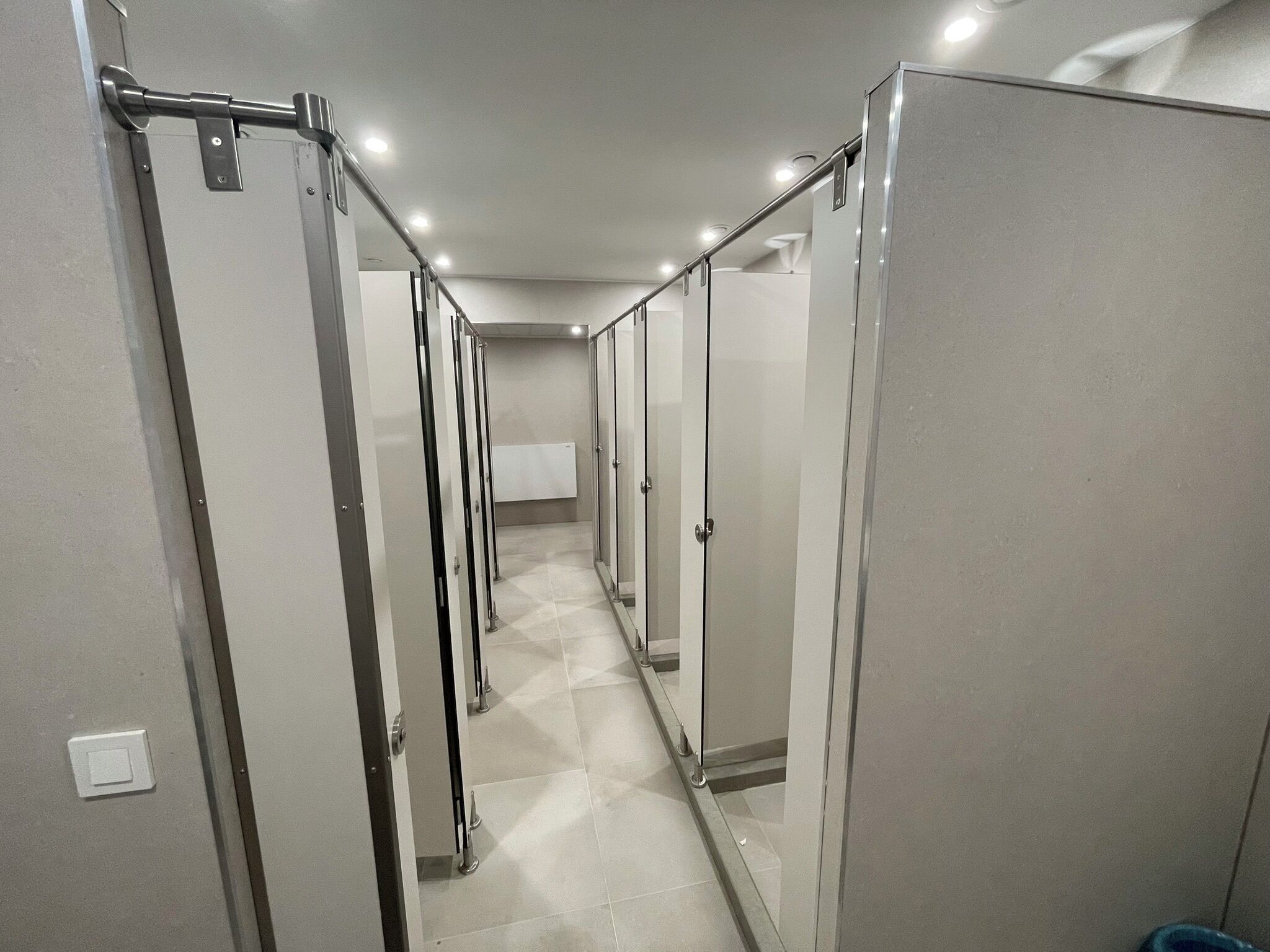 A corridor with multiple glass-enclosed stalls, each with a door and a metal handle.