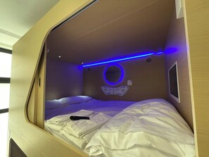 A compact, modern room with a bed, a remote control, and a circular mirror on the wall. - Urban Cube Hostel Sevilla (Seville)