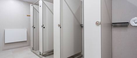 A row of white, enclosed restrooms with a metal frame and a ventilation grate on the wall.
