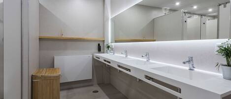 A modern bathroom with a large mirror, three sinks, and a wooden trash bin.