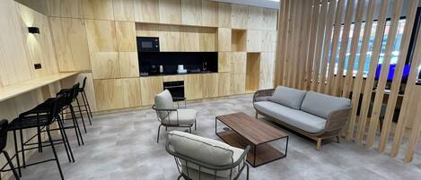 A modern living room with a sofa, chairs, a coffee table, and a kitchen area with wooden cabinets and a built-in TV.