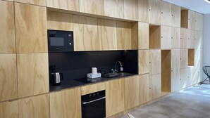 A modern kitchen with wooden cabinetry, a built-in microwave, a sink, and a dishwasher. - Urban Cube Hostel Sevilla (Seville)
