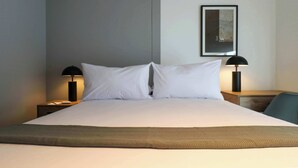 A neatly made bed with white linens, two bedside lamps, a framed picture on the wall, and a small table with a lamp beside the bed. - w* | Fabulous 2BR w/ Impressive Deco in San Isidro (San Isidro)