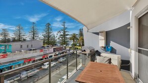 Un balcón con vista a una calle, una mesa y un ventanal con calefacción.