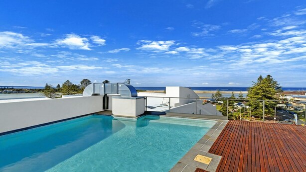 Una piscina en la azotea con vista despejada al océano y una terraza de madera.