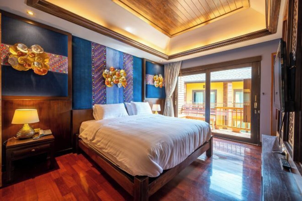 A spacious bedroom with a large bed, wooden flooring, and a balcony with a view.