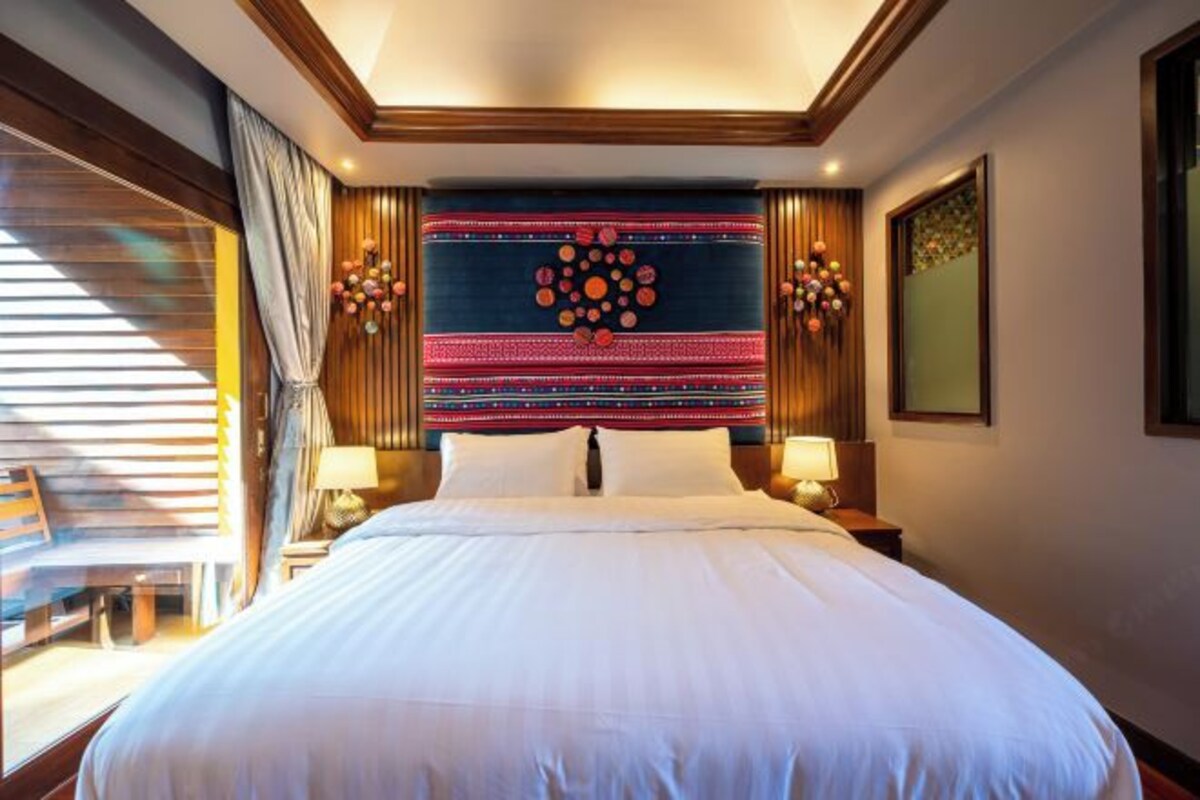 A hotel room with a large bed, a decorative headboard, two bedside lamps, and a window with blinds.