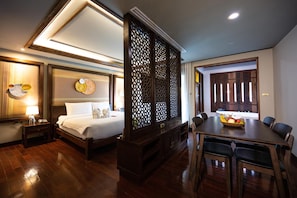 A hotel room with a bed, bedside table, lamp, decorative wall, wooden partition, and a dining area with a table and chairs. - At Gate Thaphae Hotel (Chiang Mai)