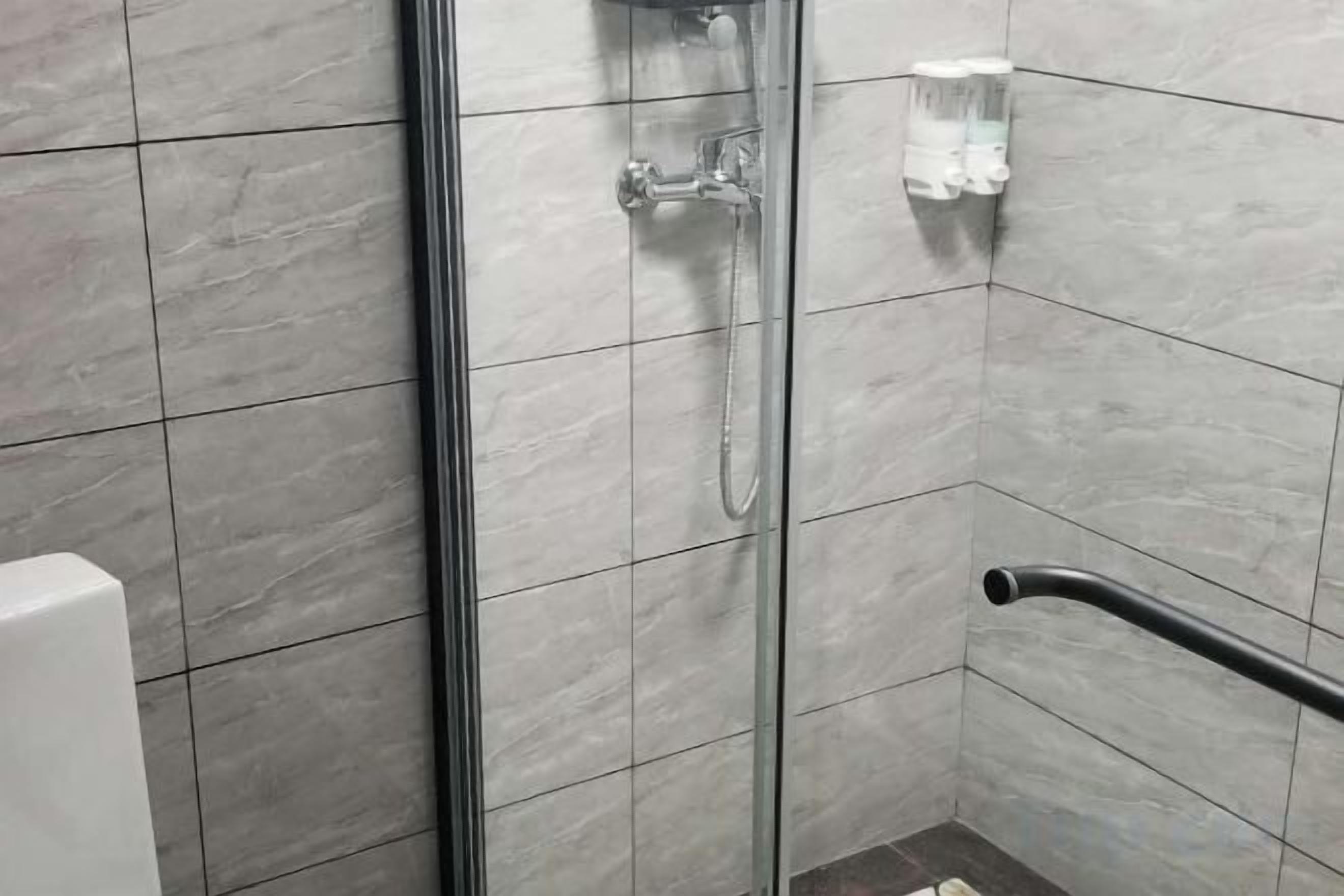 A shower area with a glass door, a handheld showerhead, and a grab bar.