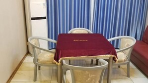Una habitación pequeña con una mesa de comedor, cuatro sillas, un sofá rojo y un equipo de aire acondicionado blanco sobre un fondo de cortina azul.