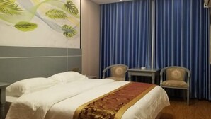 Habitación de hotel con cama, dos sillas, una mesita y una pared decorada con un mural de hojas tropicales.