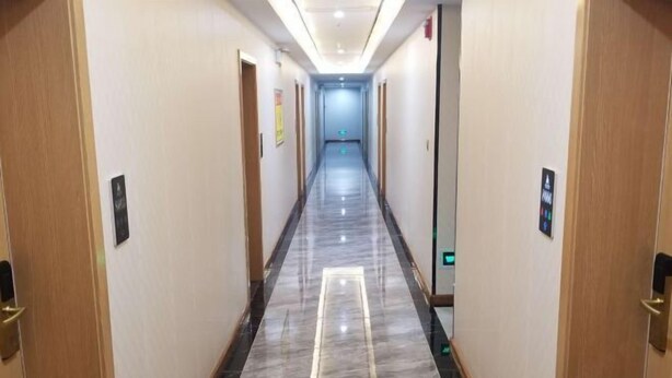 Un largo y estrecho pasillo con suelo de mármol y puertas de madera a ambos lados.