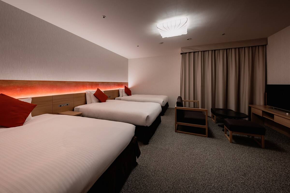 Une chambre d’hôtel avec trois lits, une télévision, un bureau et une chaise.