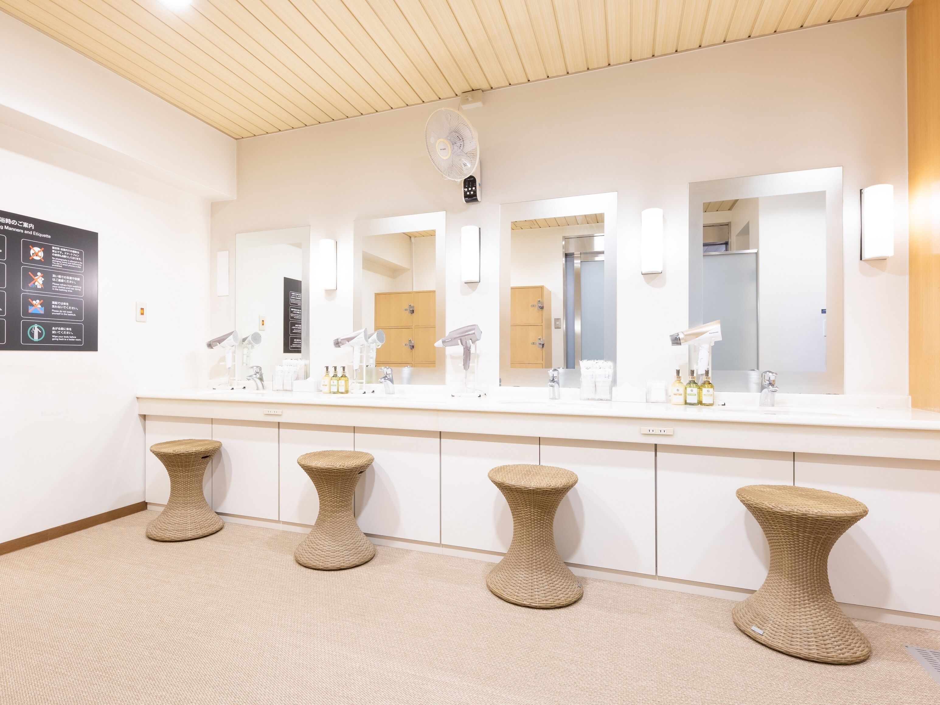 A modern bathroom with a large mirror, multiple sinks, and wicker stools.