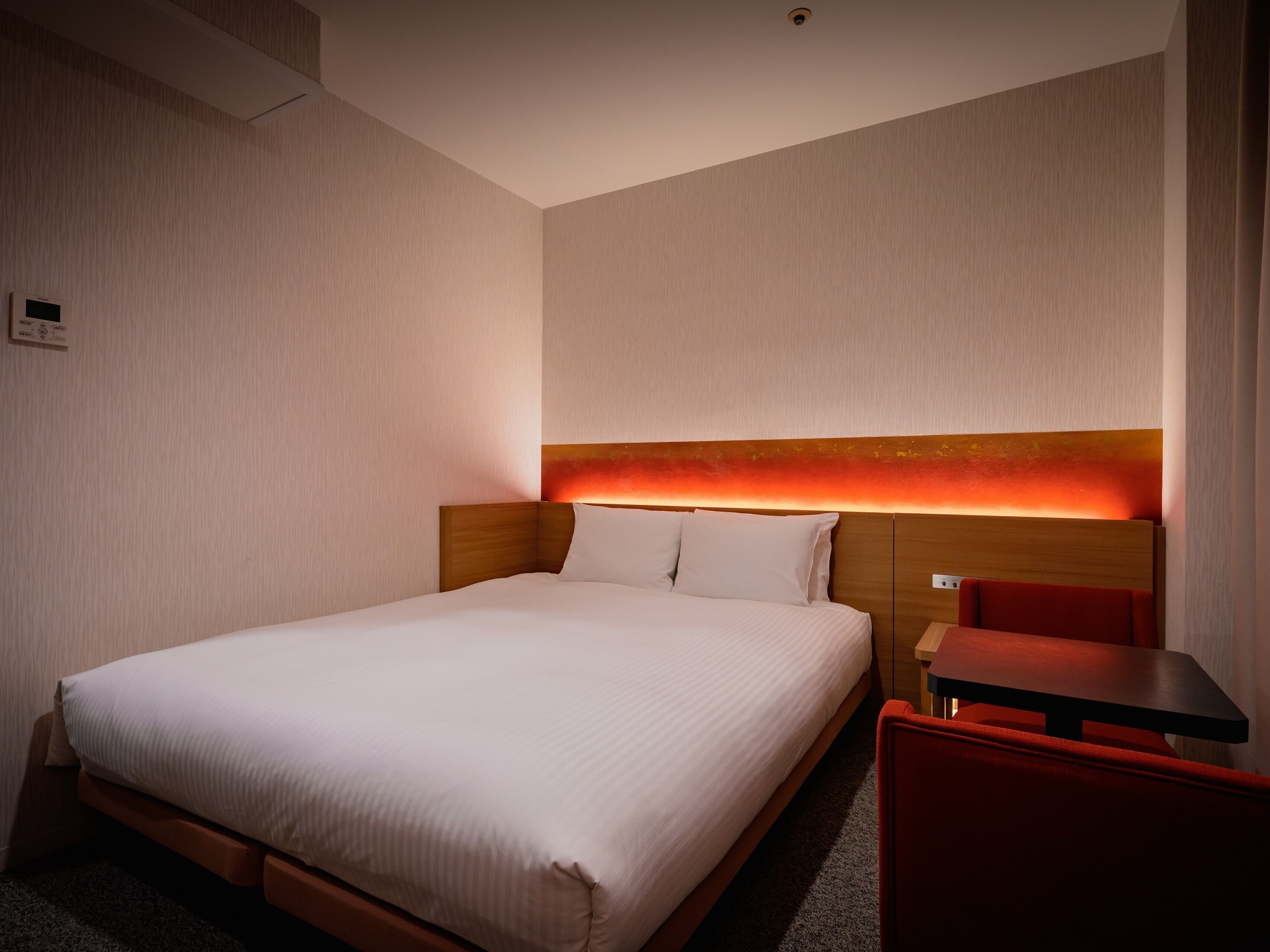 Una habitación de hotel con una cama grande, una mesita de noche y una silla roja.