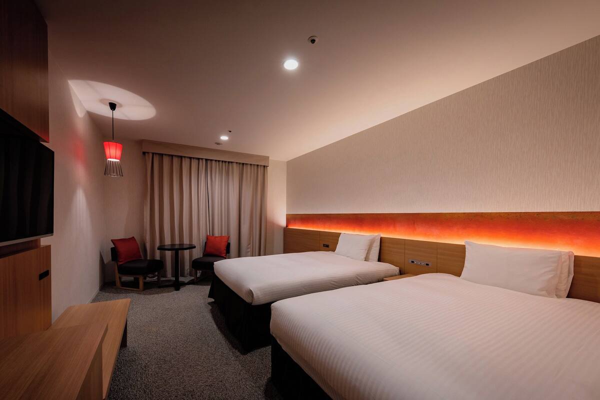 Une chambre d’hôtel avec deux lits, une télévision, un bureau, une chaise et une lampe.