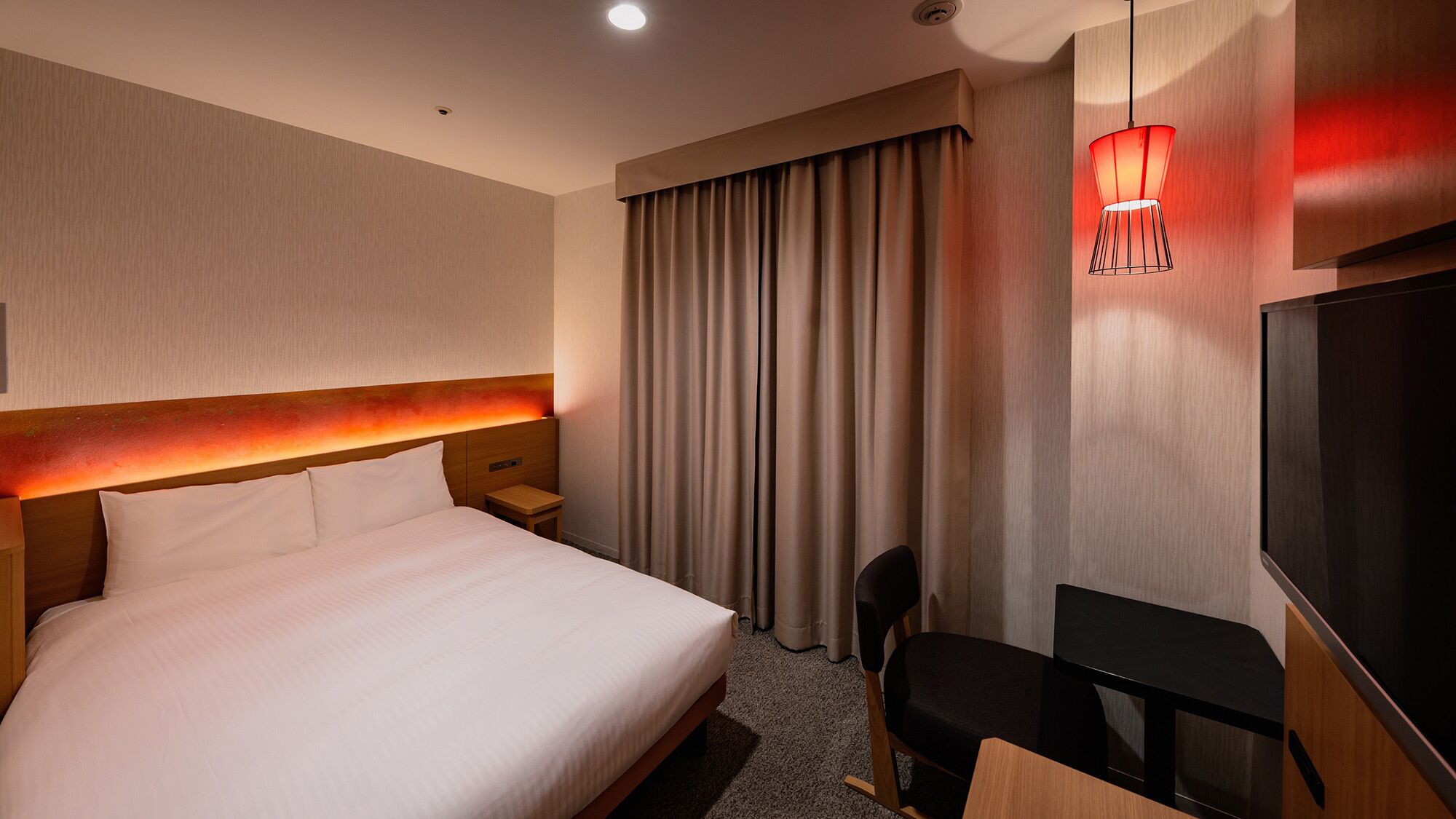 Ein Hotelzimmer mit einem großen Bett, einem Schreibtisch, einem Sessel, einem Fernseher und einem Fenster mit Vorhängen.