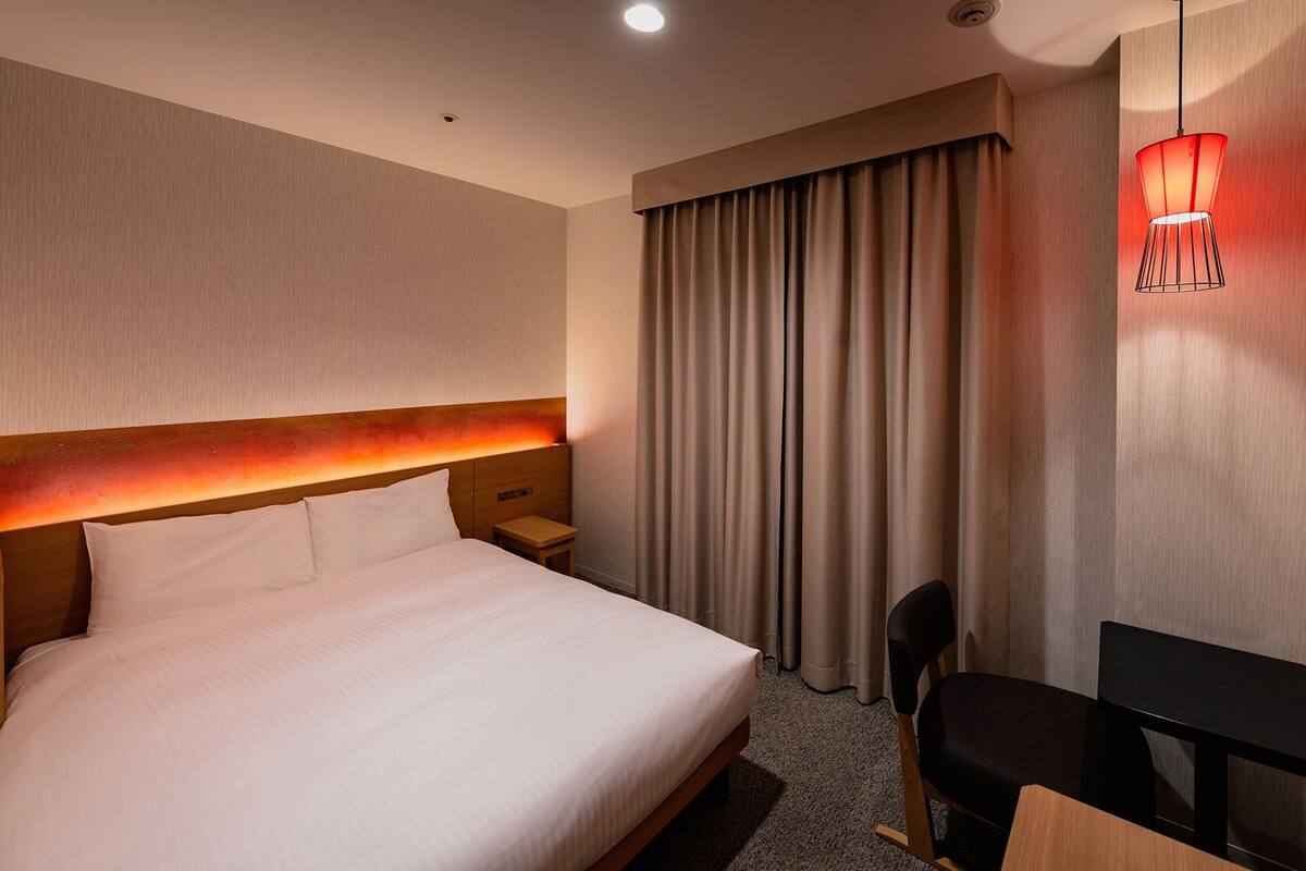 Une chambre d’hôtel avec un grand lit, un bureau, une chaise, une télévision et une fenêtre avec des rideaux.
