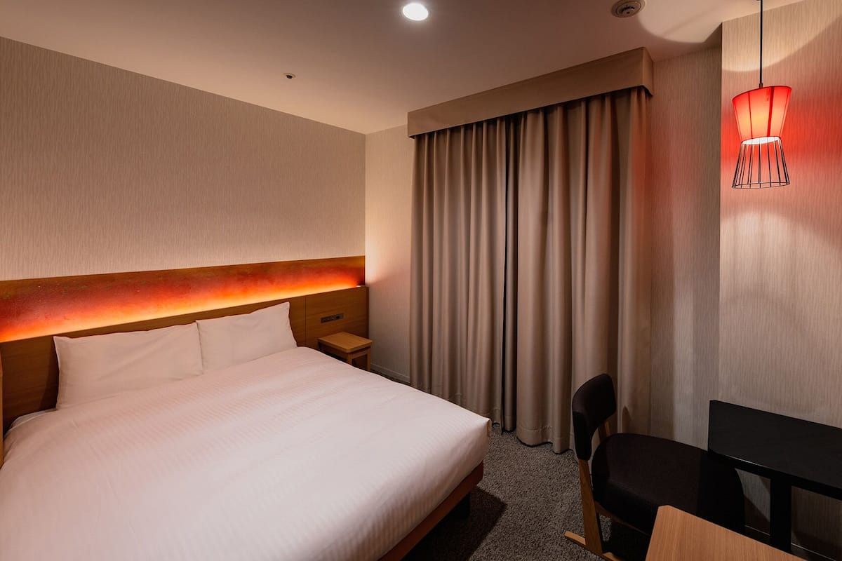 A hotel room with a large bed, a desk, a chair, a TV, and a window with curtains.