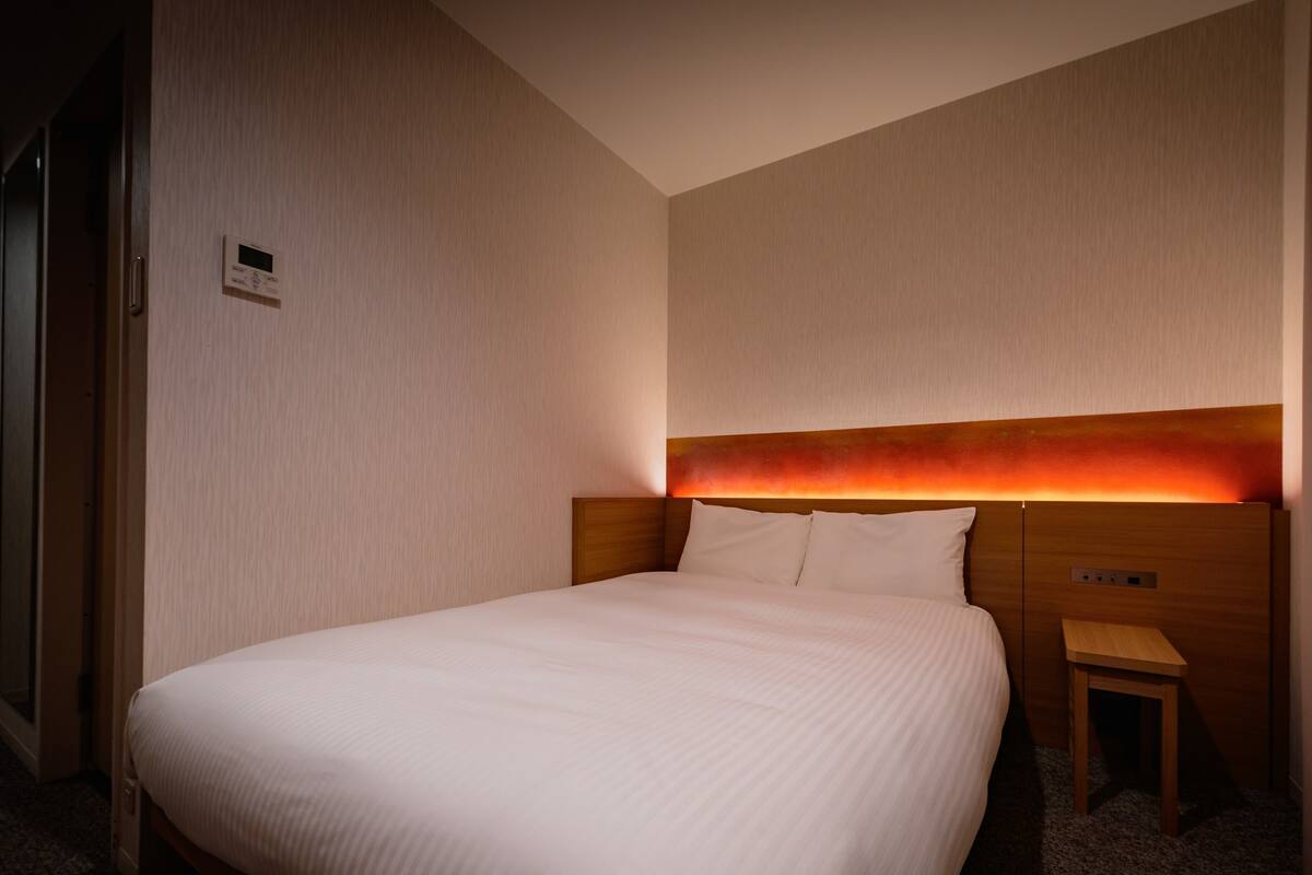 Une chambre d’hôtel avec un grand lit, une table de chevet et un thermostat fixé au mur.