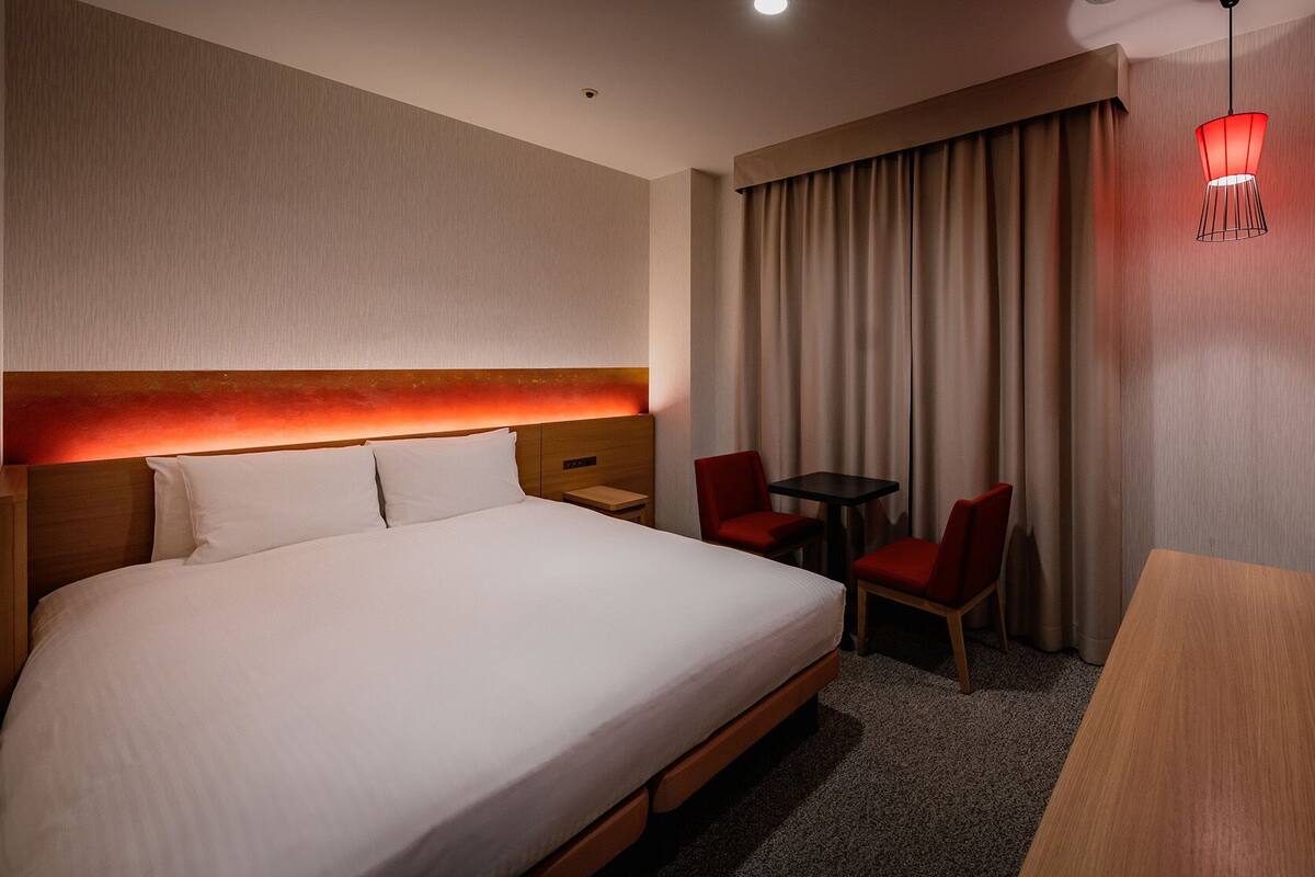 Une chambre d’hôtel avec un grand lit, un bureau, deux chaises, une télévision et une lampe suspendue rouge.