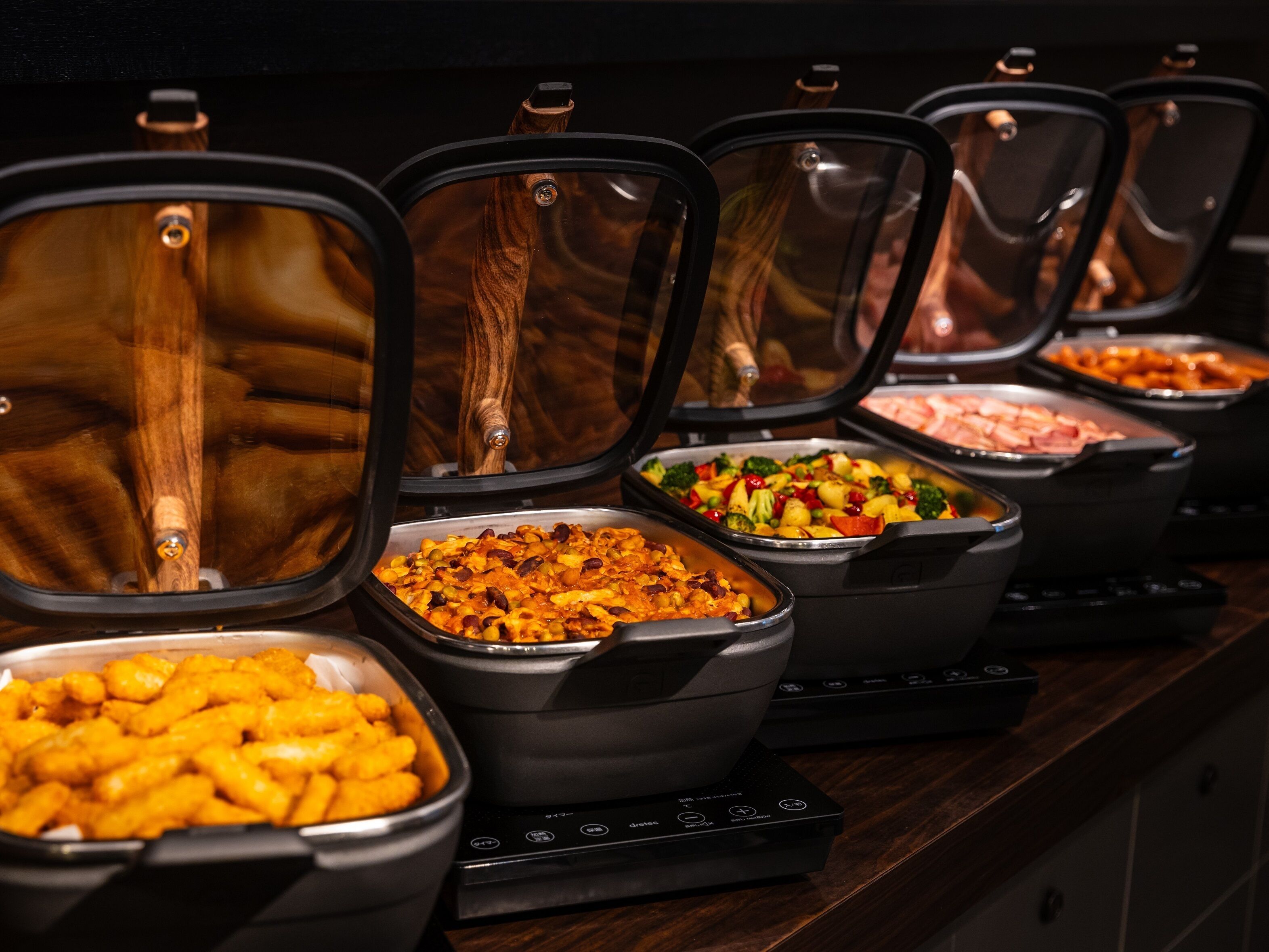 A buffet with various food options in black containers, including pasta, vegetables, and meats.