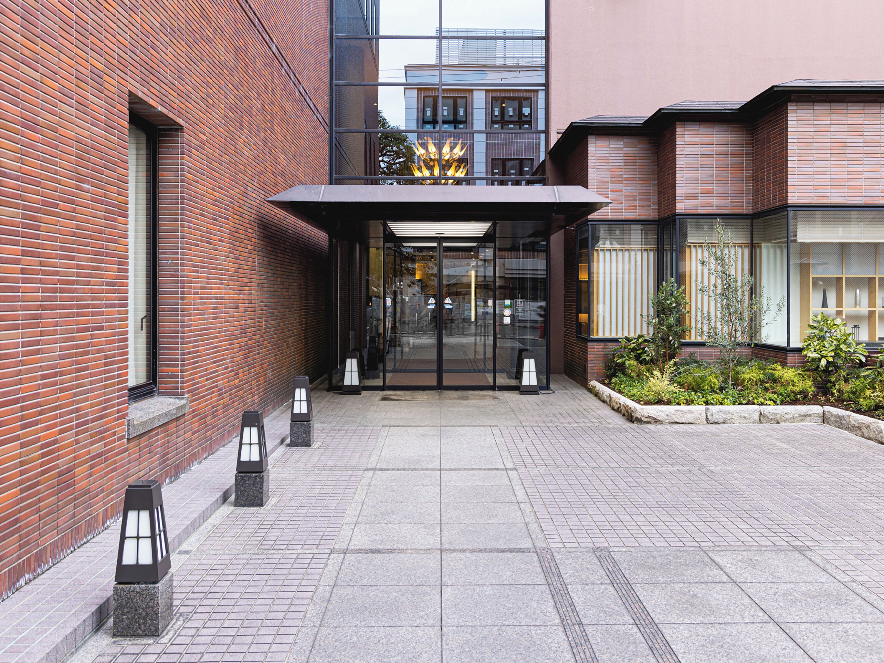 Un edificio moderno con fachada de ladrillo, entrada de cristal y un peque ño jardín con plantas.