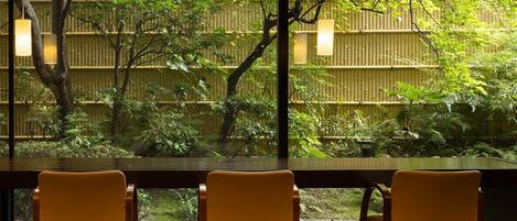 Un comedor con tres sillas y una mesa, con vistas a una valla de bambú y abundante vegetación.