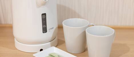 A white electric kettle with a digital display, two white cups, and a small white plate with tea packets.