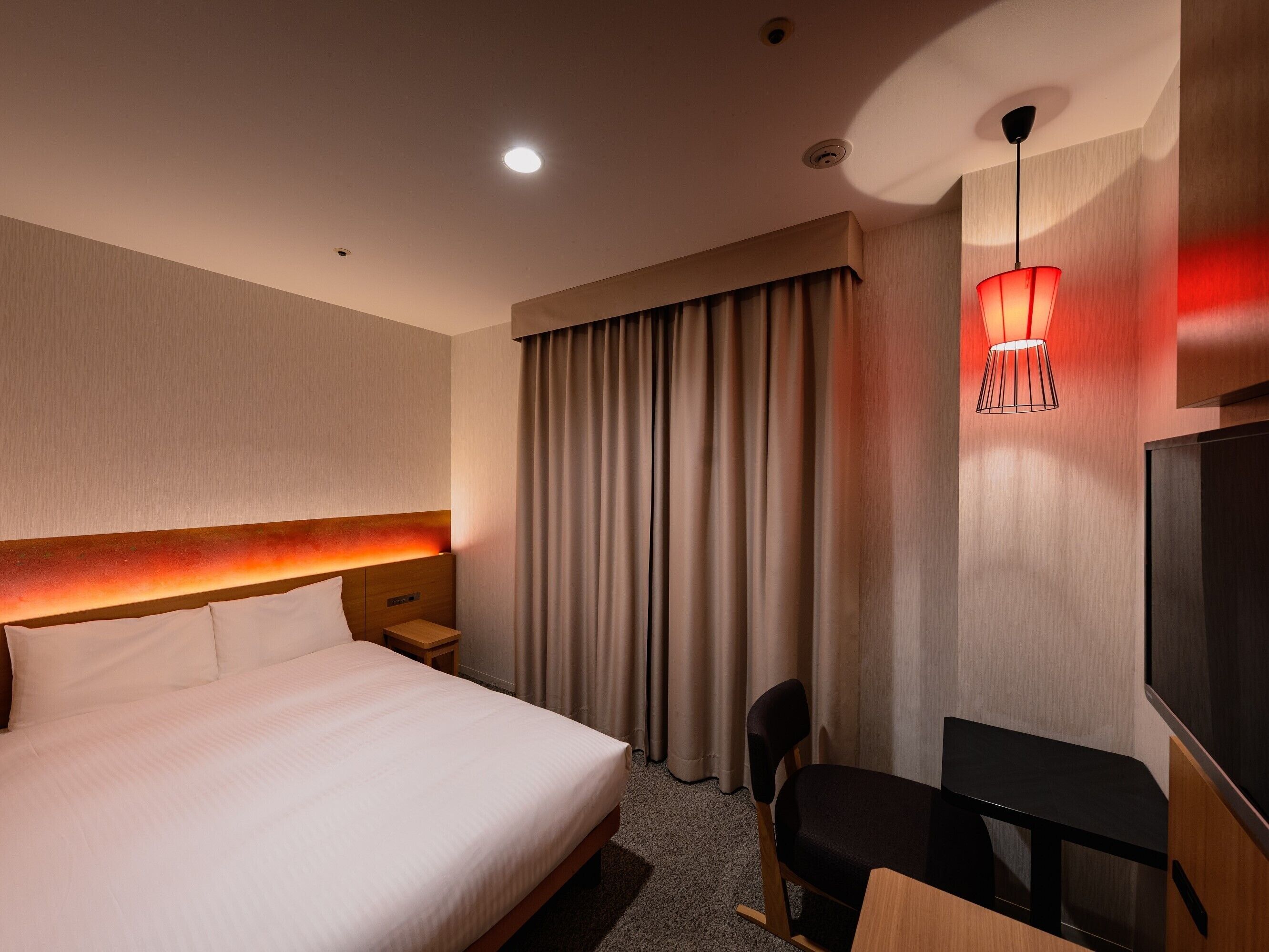 Une chambre d’hôtel avec un grand lit, un bureau, une chaise, une télévision et une lampe rouge.