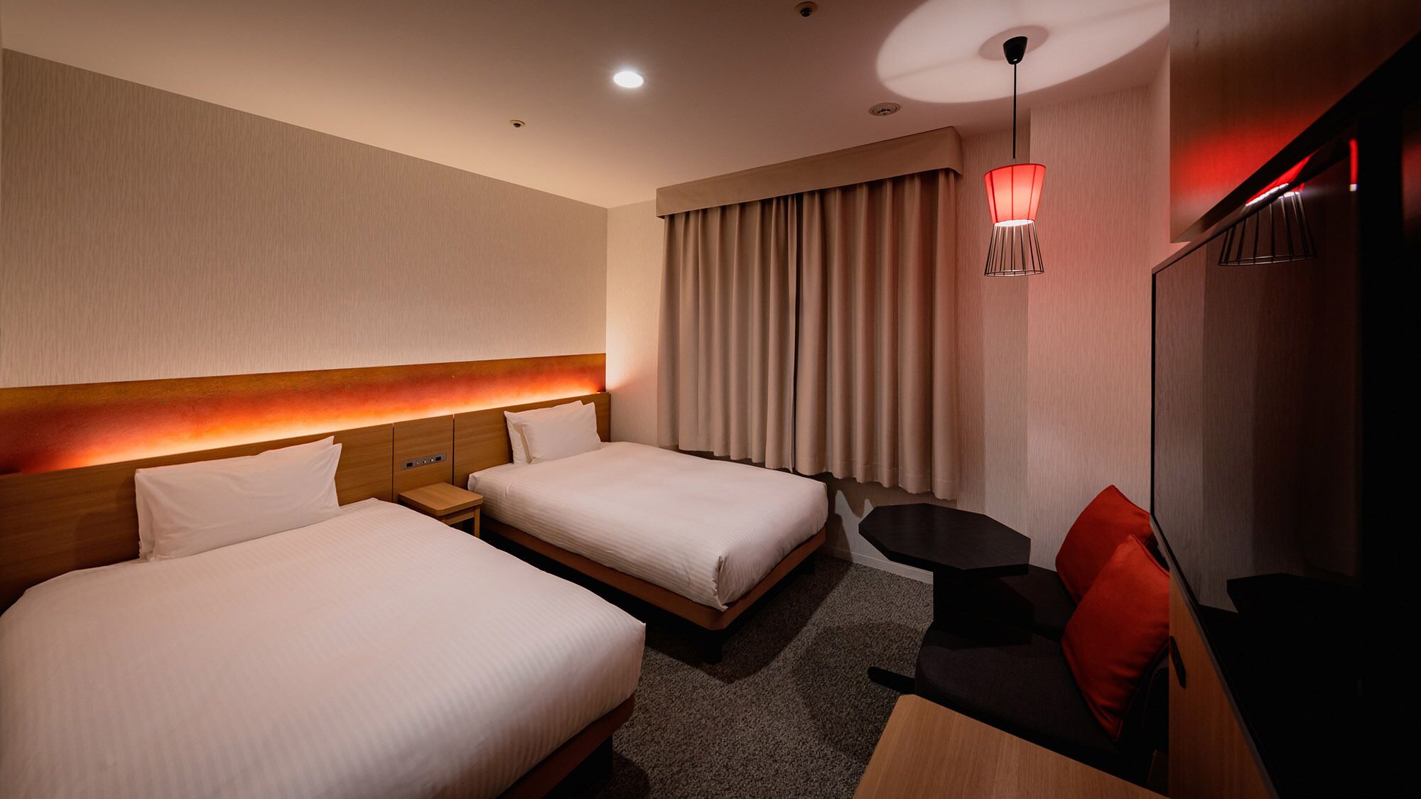 Ein Hotelzimmer mit zwei Betten, einem kleinen Tisch, einem Stuhl, einem Schreibtisch und einem Fernseher.