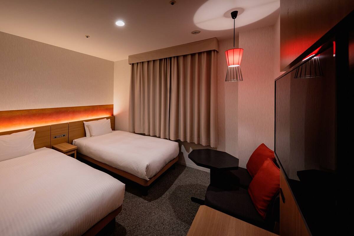 Une chambre d’hôtel avec deux lits, une petite table, une chaise, un bureau et un téléviseur.