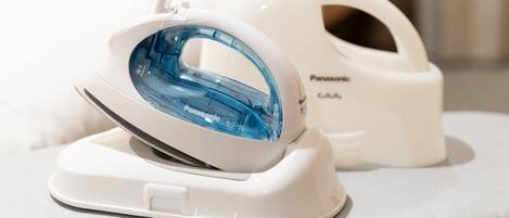 A Panasonic iron with a blue water tank and a white iron, both placed on a white surface.