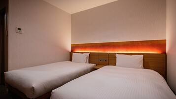 Una habitación de hotel con dos camas individuales, un cabecero de madera con luz integrada y un panel de control en la pared.