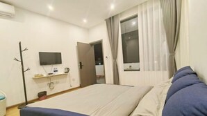 A bedroom with a bed, a TV mounted on the wall, a window with curtains, and a door leading to another room. - Fushui Inn (Dali City)