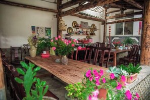 A rustic dining area with a wooden table, chairs, and potted plants.