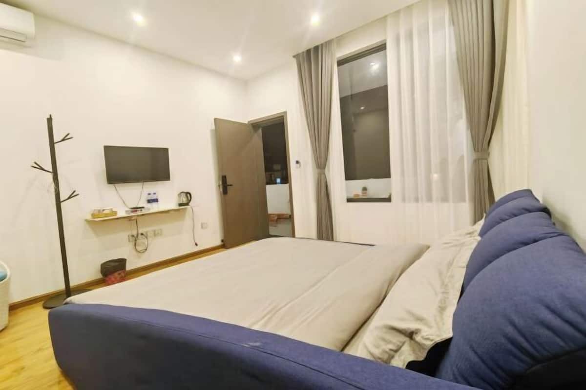 A bedroom with a bed, a TV mounted on the wall, a window with curtains, and a door.