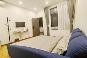 Un dormitorio con cama, televisor montado en la pared, ventana con cortinas y puerta.