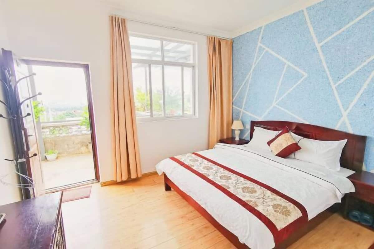 A bedroom with a bed, a nightstand, a window with curtains, and a view of greenery outside.