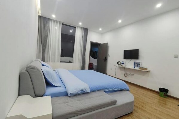 Un dormitorio moderno con cama, televisor montado en la pared y ventana con cortinas.