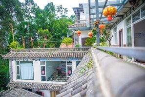 A traditional building with a tiled roof, a balcony, and a view of a forested area.