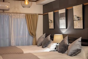 Quarto de hotel com duas camas, uma janela grande com cortinas, ar condicionado fixado na parede e três quadros abstratos.
