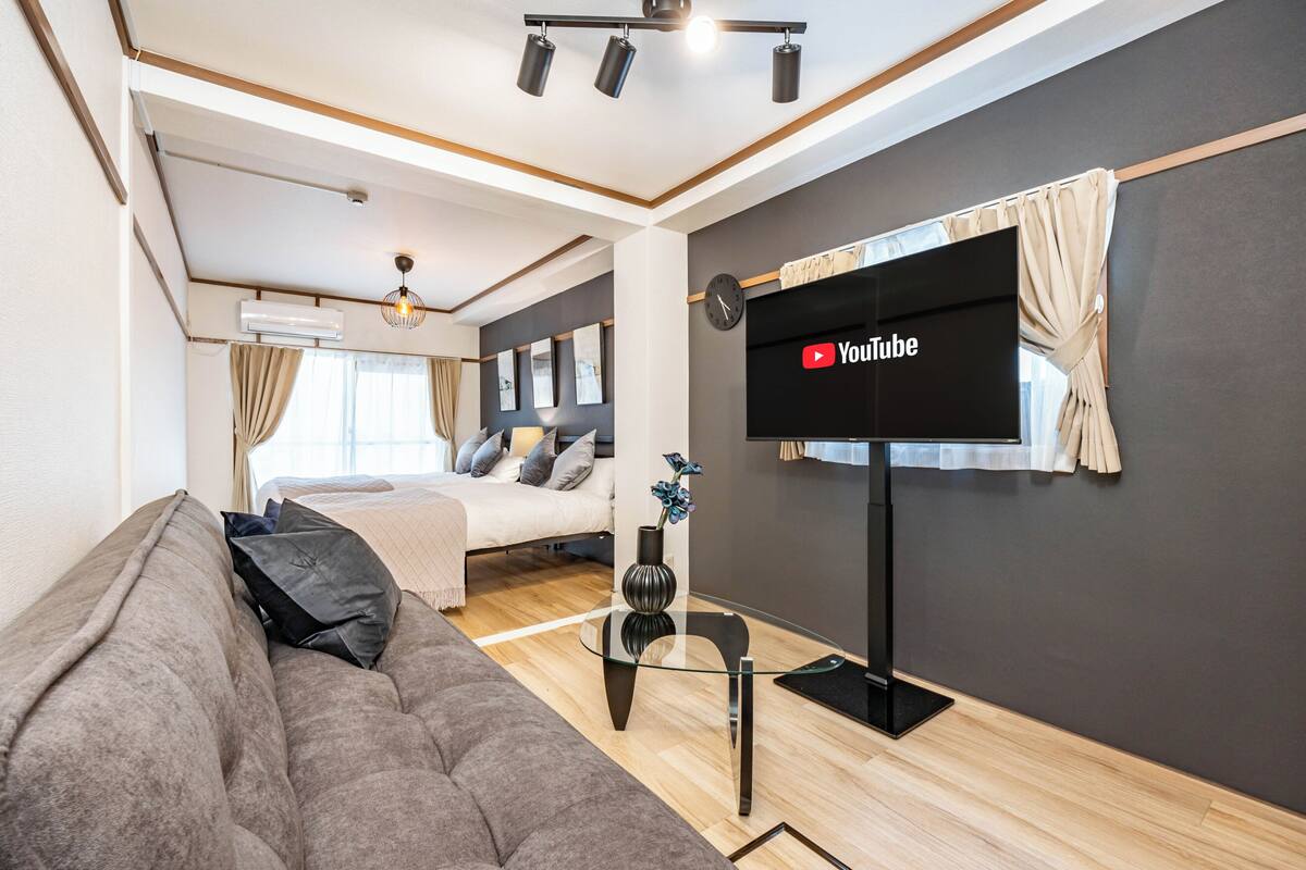 Un salon moderne avec un canapé, une table basse en verre, un téléviseur à écran plat fixé au mur et un luminaire suspendu au plafond.