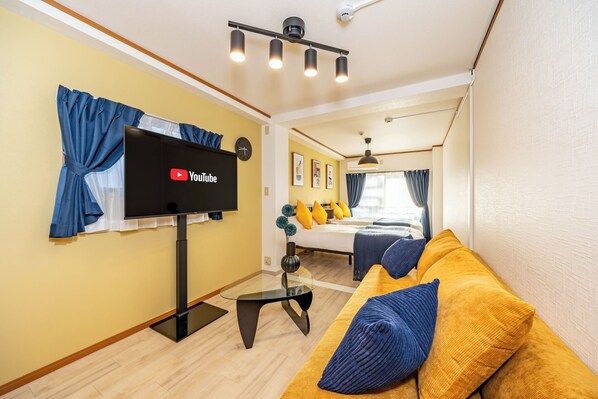 Uma sala de estar moderna com uma TV de tela plana, um sofá com almofadas azuis e uma mesa de centro de vidro.